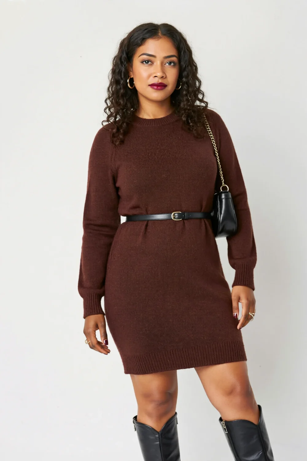 Woman in a burgundy sweater dress with slim belt and black knee-high boots, styled with a shoulder bag for polished party-ready looks