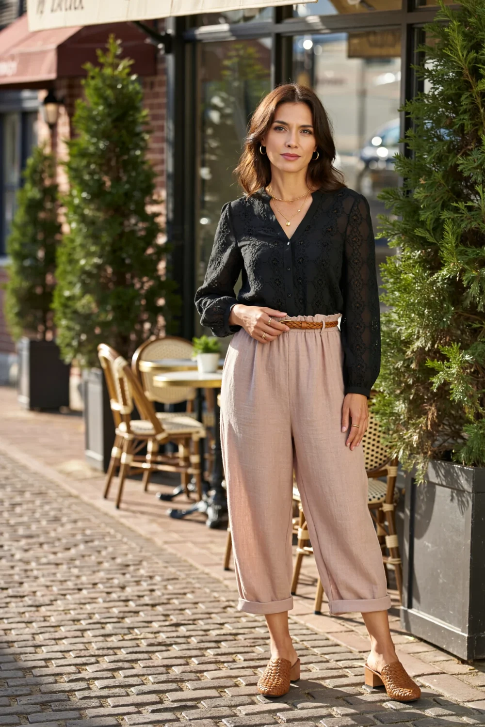 Woman in a black eyelet shirt tucked into taupe paperbag-waist linen culottes with braided belt, rolled cuffs and woven mules.
