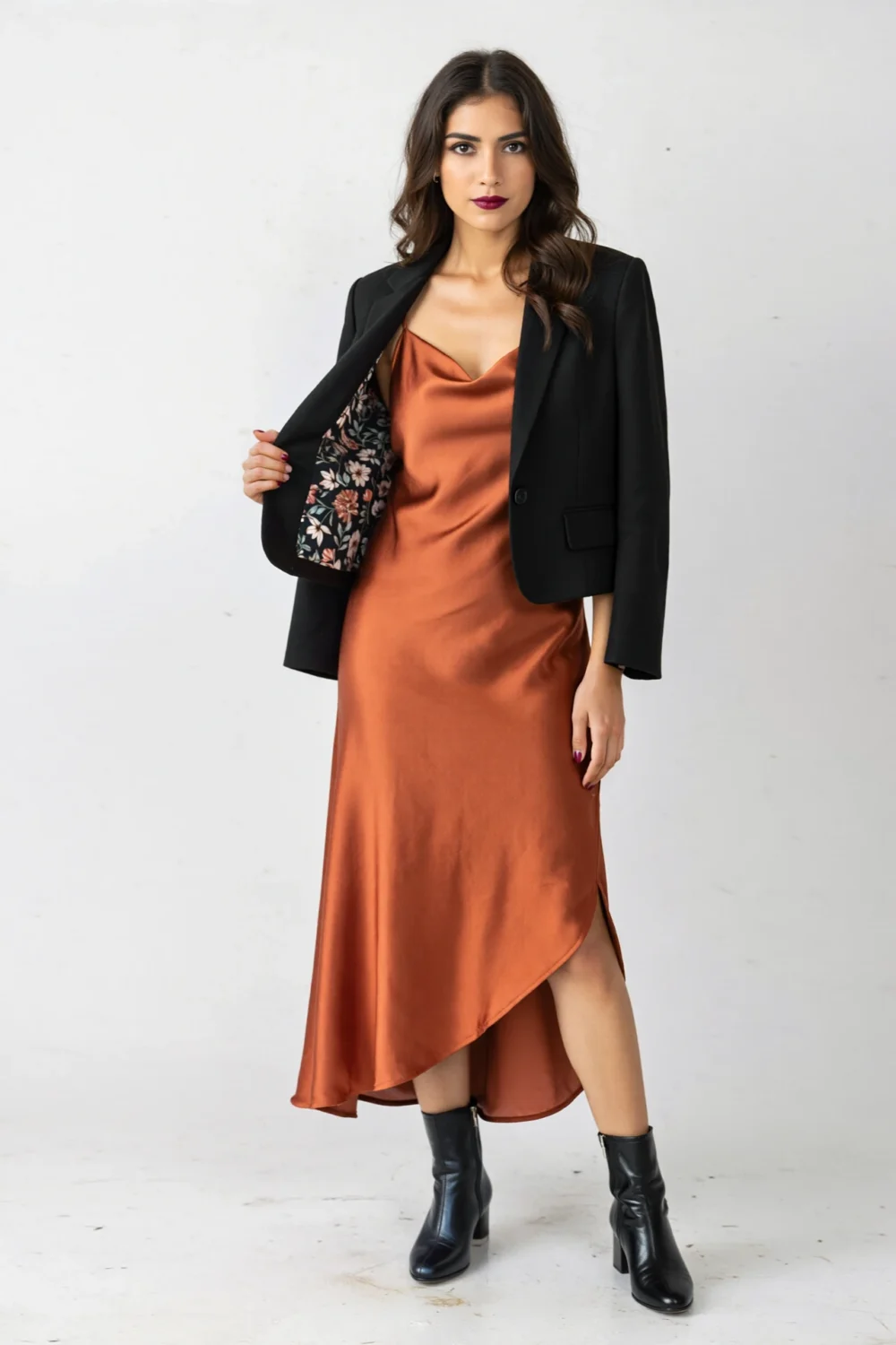 Terracotta satin slip dress with cropped black blazer and boots, creating a chic autumn wedding look with city-ready contrast