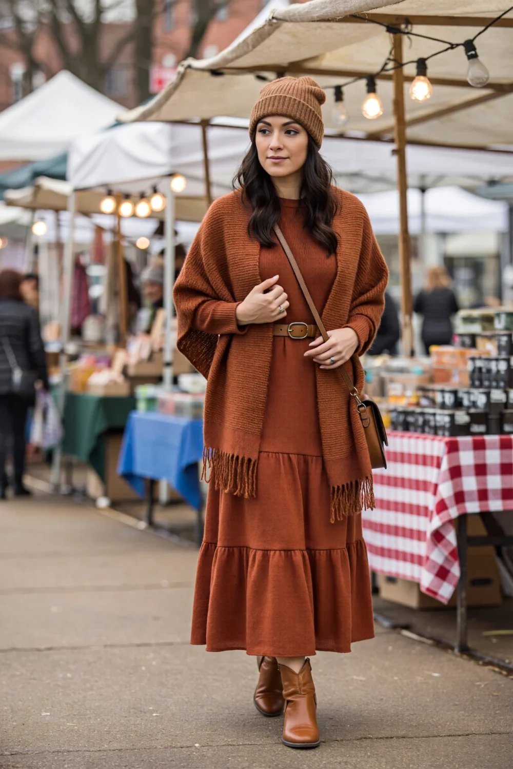 Woman at a market in a rust tiered maxi, oversized scarf wrap cinched with a belt, leather ankle boots, crossbody bag and beanie