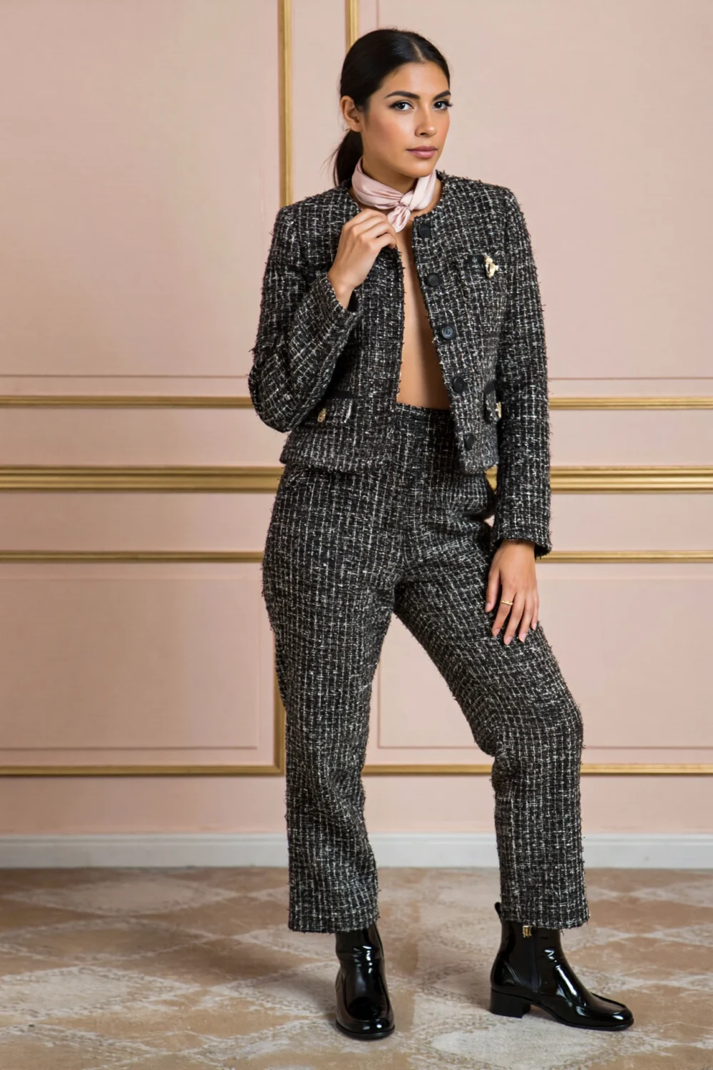 Woman in textured black tweed cropped jacket and slim trousers, styled with a silk scarf and patent ankle boots, exuding warmth.