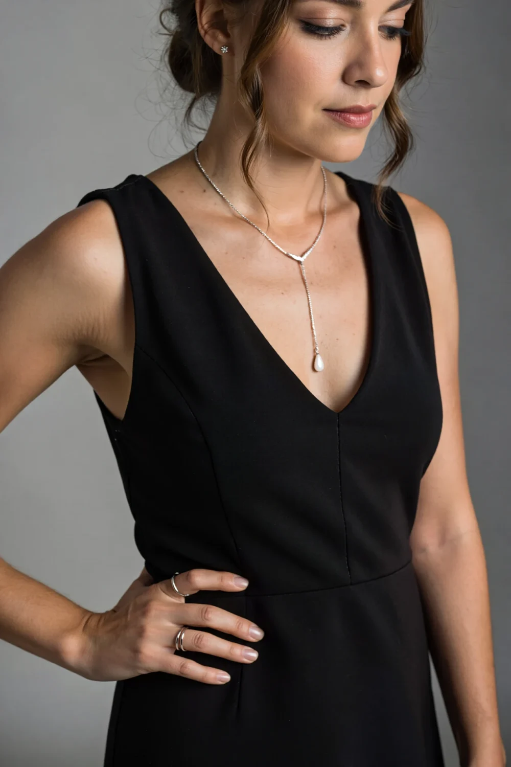 Woman in black V-neck dress wearing a silver Y-lariat necklace with a slim drop teardrop, minimal stud earrings and fine rings
