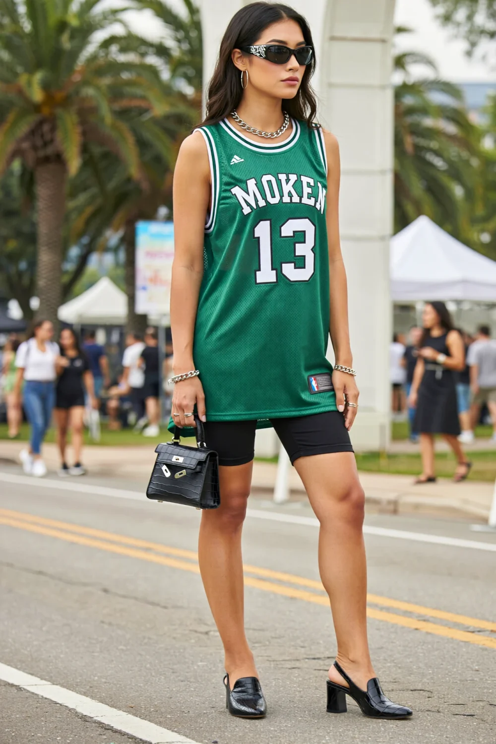 Street-style model in oversized green basketball jersey over biker shorts, with black slingbacks, croc bag, and silver jewelry accents
