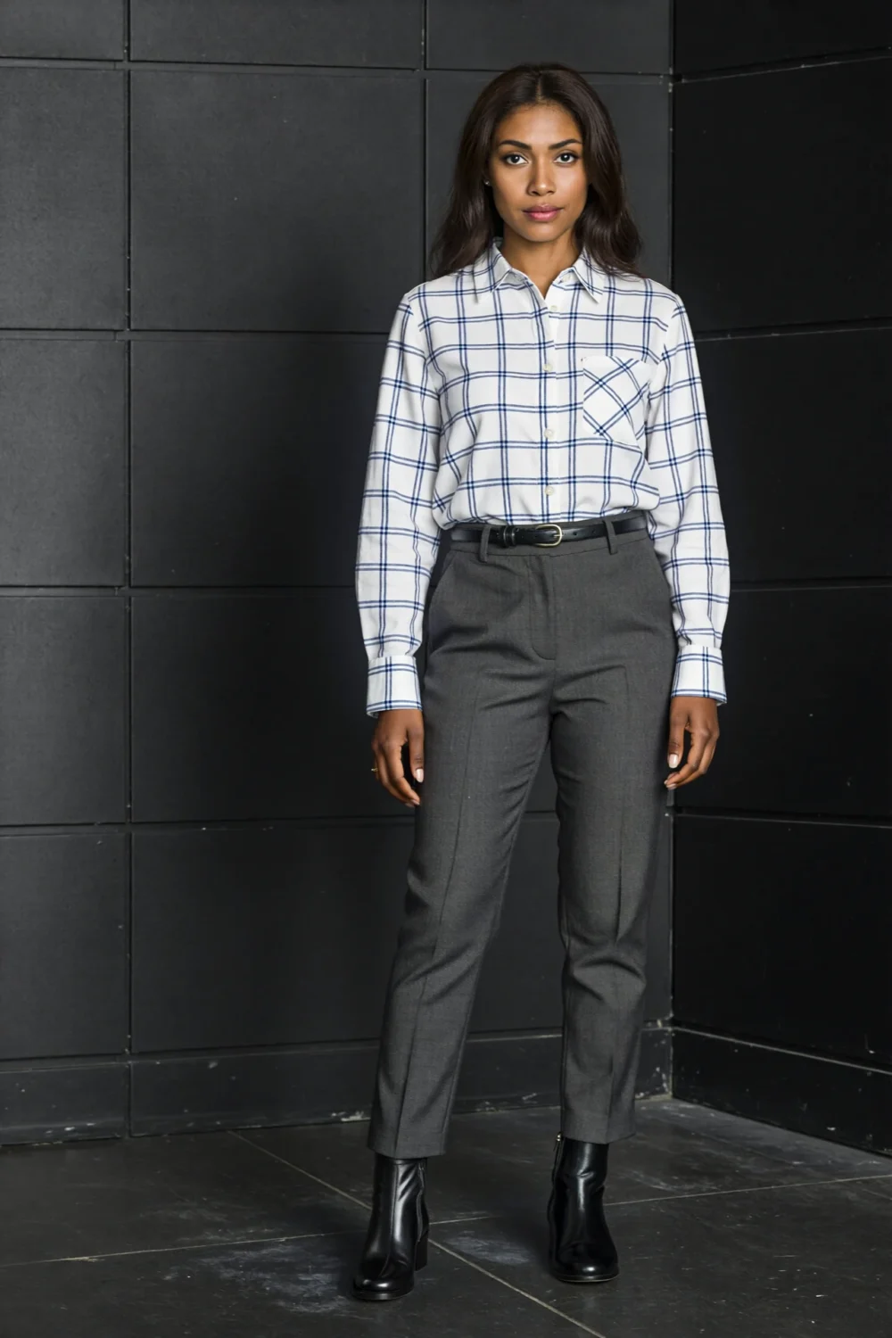 Woman wearing a white windowpane shirt with charcoal trousers, slim belt, and black boots, creating a sleek minimalist outfit.