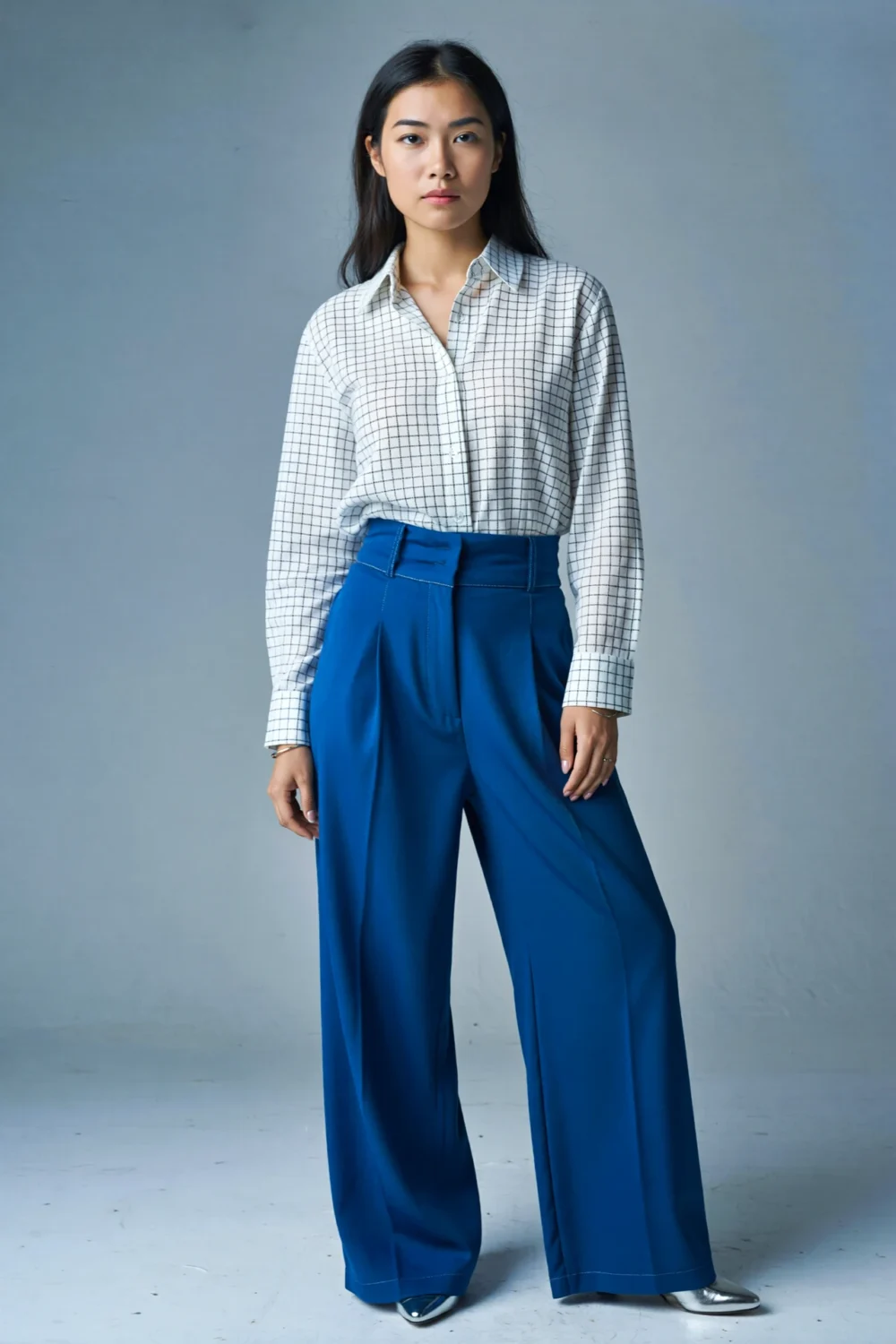 Woman in a windowpane shirt with cobalt wide-leg trousers, styled minimally with metallic shoes for a clean, modern architectural look