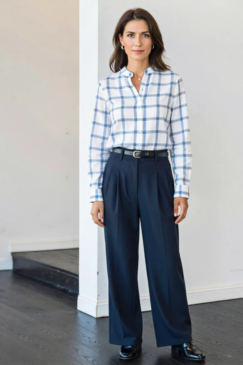 Woman wearing a white windowpane shirt tucked into navy pleated trousers with belt, polished meeting-ready business-casual outfit